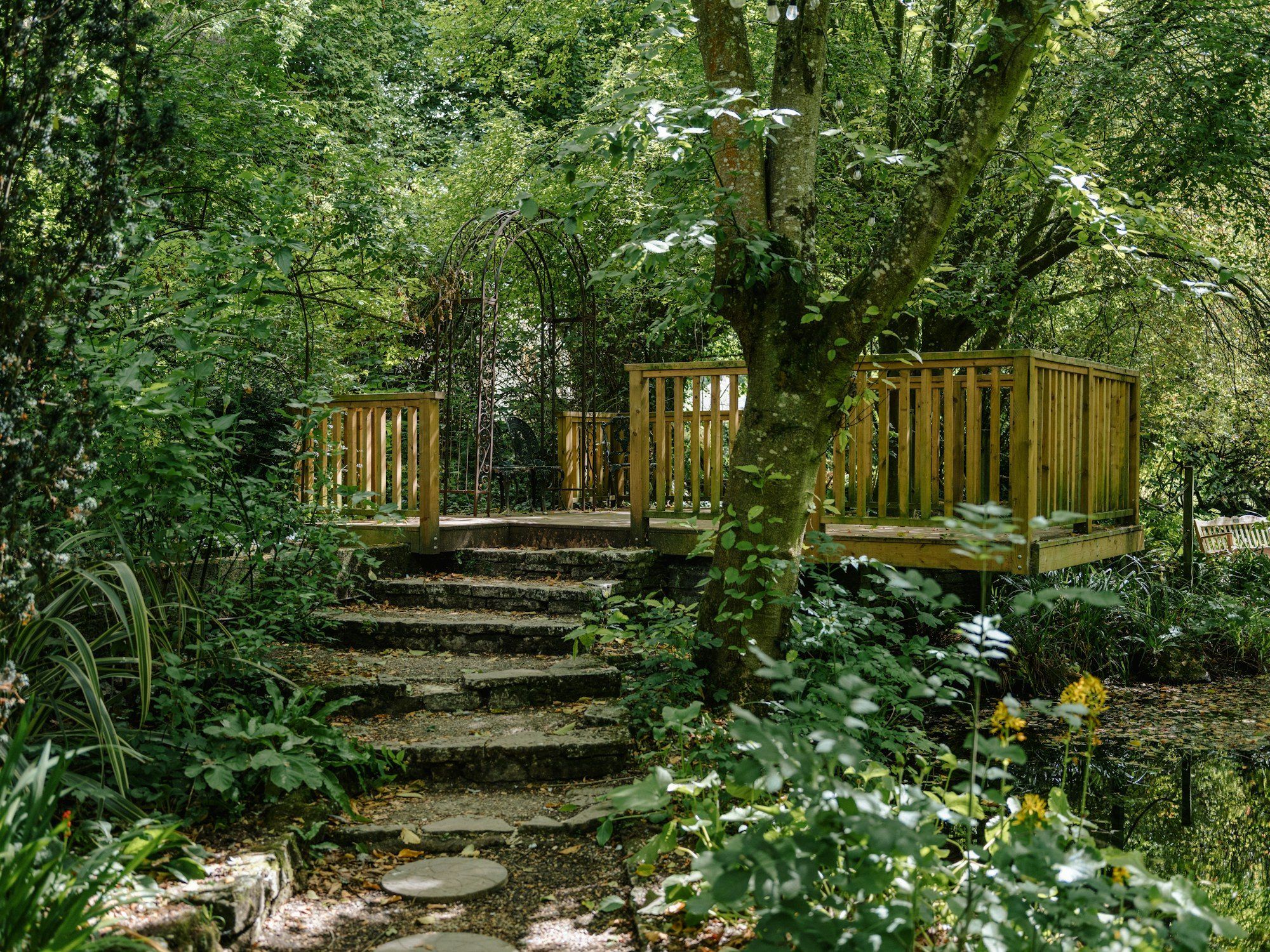 Raised timber deck with railings reached by stone steps in a leafy garden