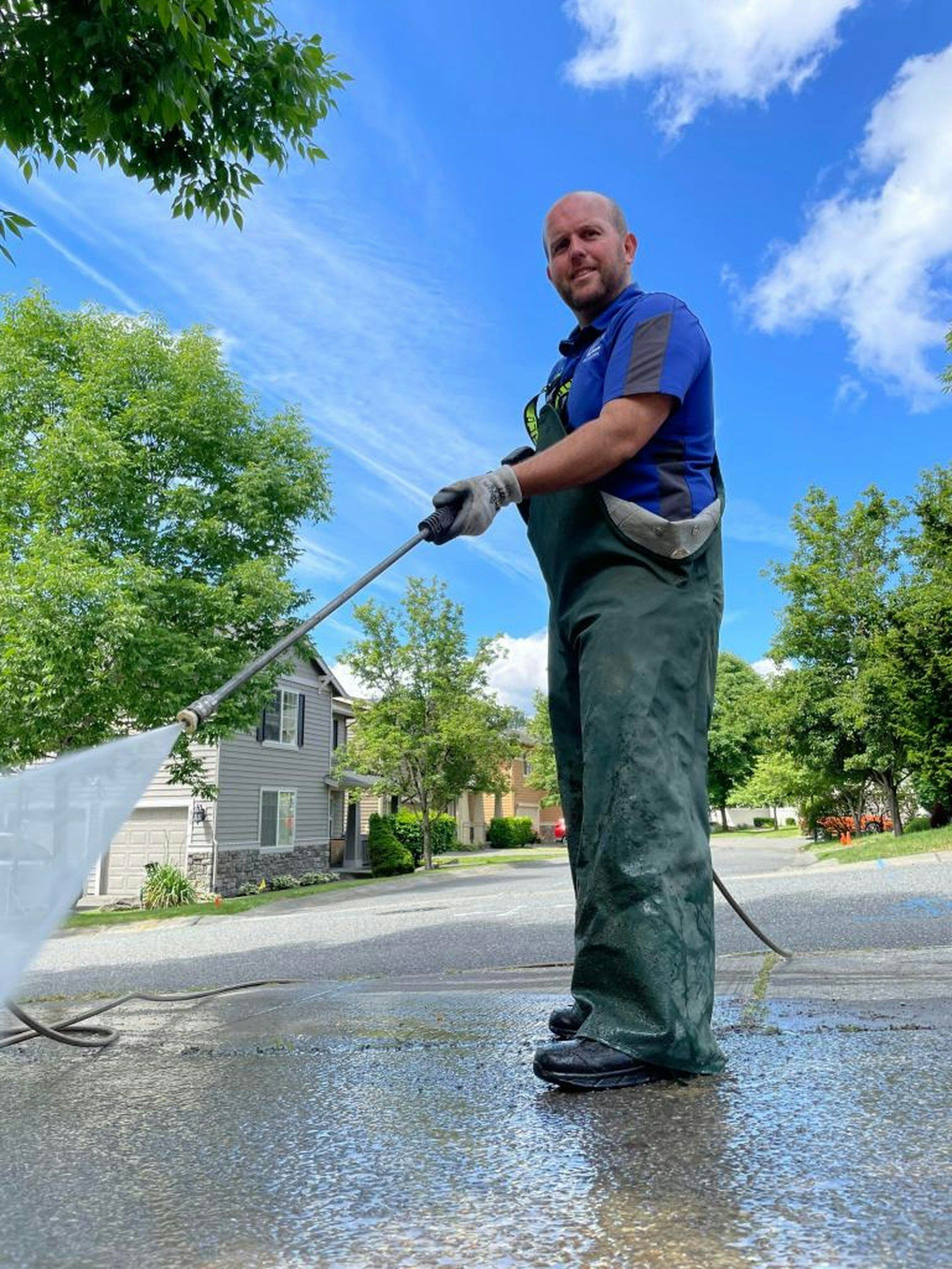 Man in waterproofs pressure washing a driveway on a sunny day