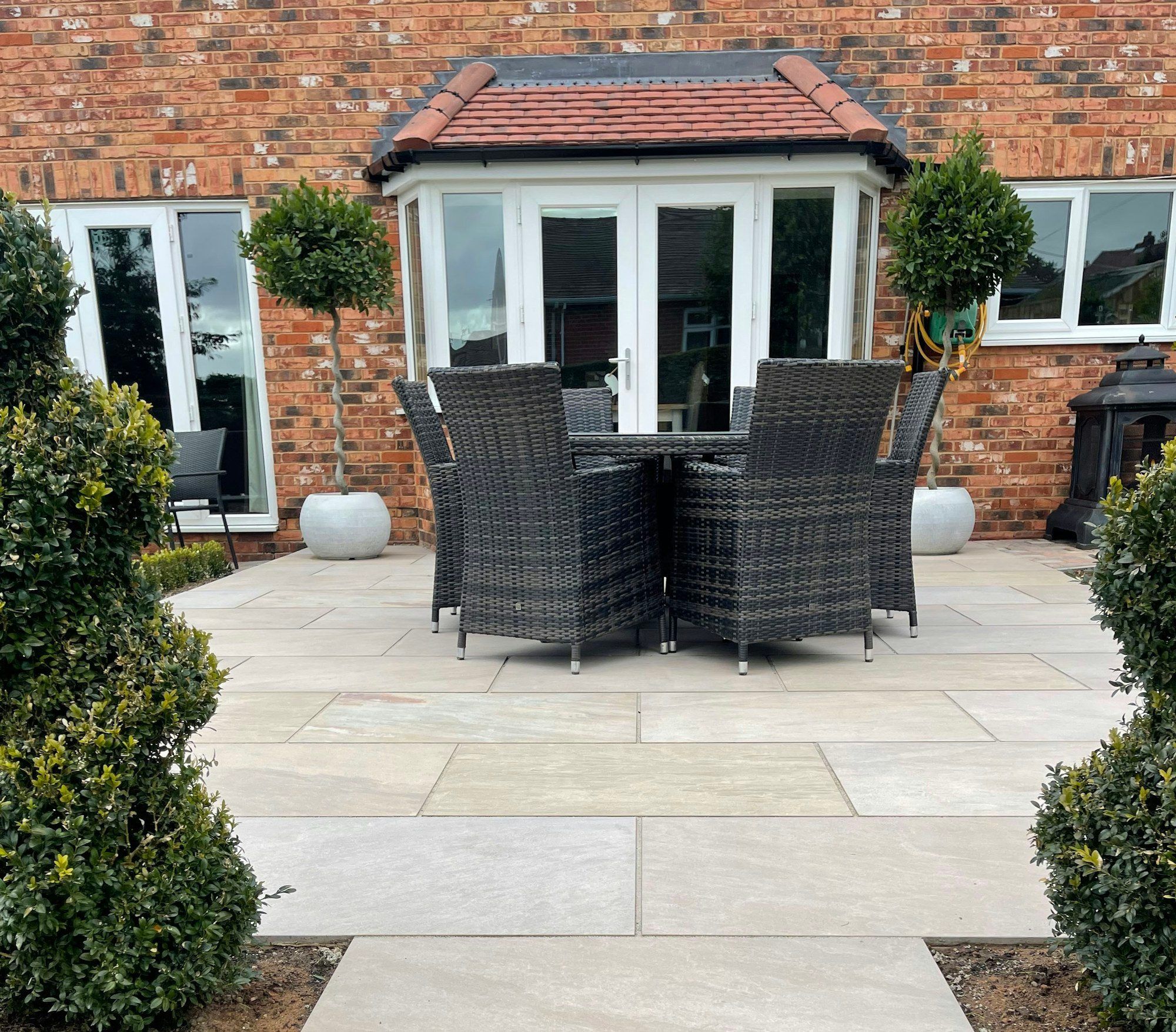 Light sandstone patio with garden furniture outside a red-brick house